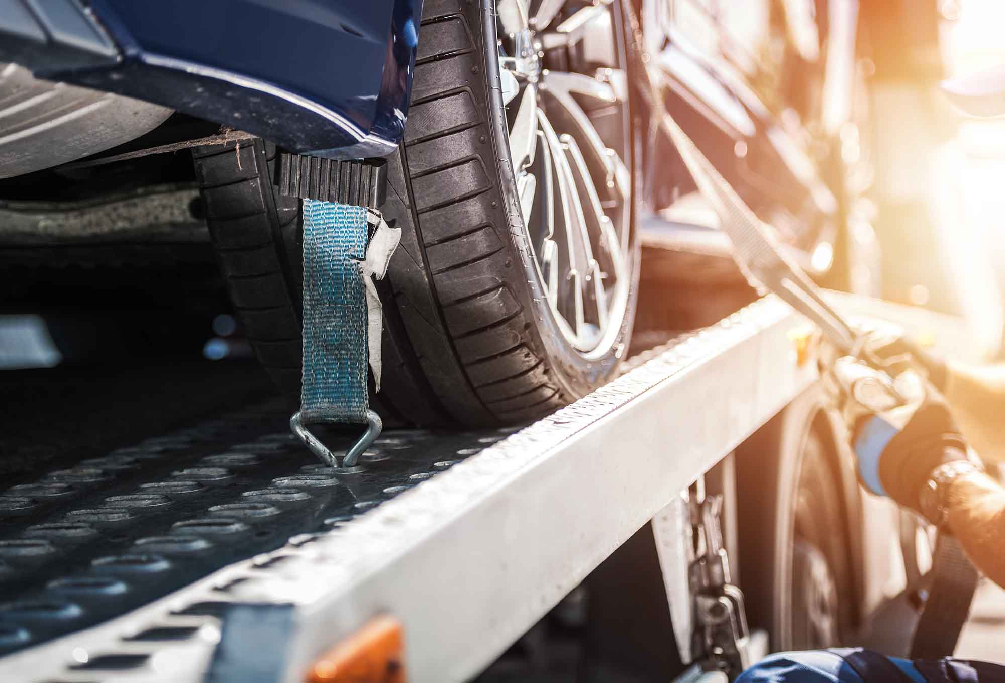 towing services auto repair - car being strapped to tow truck 